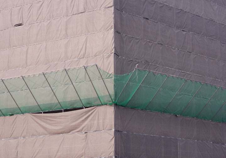 Building under construction covered with grey protective netting, featuring green System T safety nets installed mid-facade.